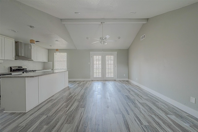 kitchen with white cabinets, wall chimney exhaust hood, vaulted ceiling with beams, and light wood-type flooring