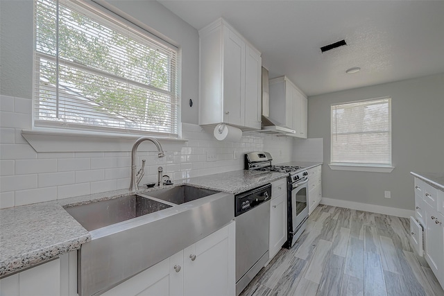 kitchen featuring light stone countertops, tasteful backsplash, wall chimney exhaust hood, stainless steel appliances, and white cabinets