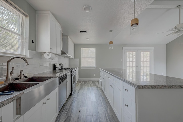 kitchen featuring a textured ceiling, stainless steel appliances, stone countertops, a center island, and white cabinetry