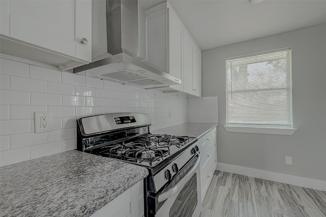 kitchen with backsplash, white cabinets, stainless steel gas range, wall chimney exhaust hood, and light stone countertops