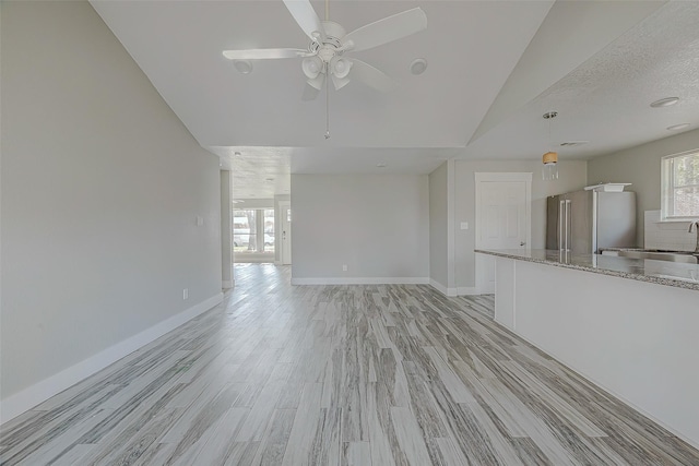 unfurnished living room featuring lofted ceiling, ceiling fan, light wood-type flooring, and a textured ceiling