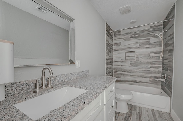 full bathroom with tiled shower / bath combo, a textured ceiling, toilet, vanity, and hardwood / wood-style flooring