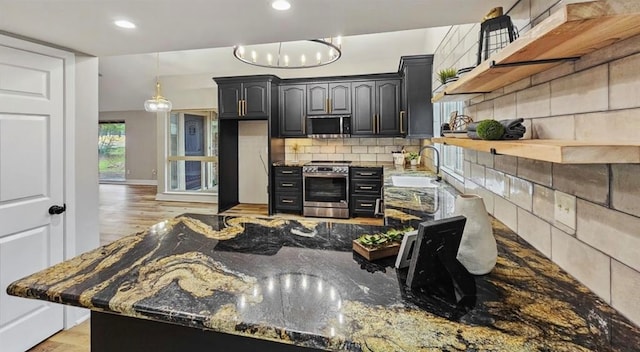 kitchen featuring stainless steel appliances, light hardwood / wood-style flooring, dark stone counters, and sink