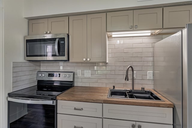 kitchen with decorative backsplash, appliances with stainless steel finishes, gray cabinetry, sink, and butcher block counters