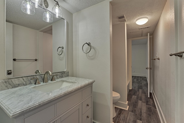 bathroom featuring vanity, wood-type flooring, a textured ceiling, and toilet