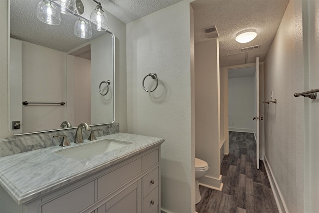 12900 Walden Rd Unit 105A, Montgomery, TX 77356 - bathroom featuring a textured ceiling, wood finished floors, toilet, vanity, and a textured wall