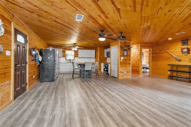 interior space featuring a breakfast bar area, wooden walls, white cabinets, black appliances, and light wood-type flooring