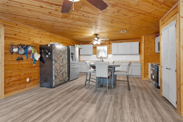 dining room featuring ceiling fan, light wood-type flooring, wooden walls, and wooden ceiling