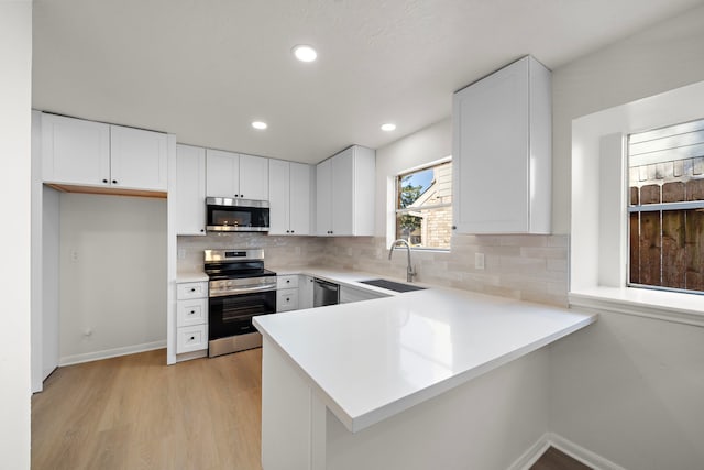 kitchen with kitchen peninsula, appliances with stainless steel finishes, sink, light hardwood / wood-style flooring, and white cabinets