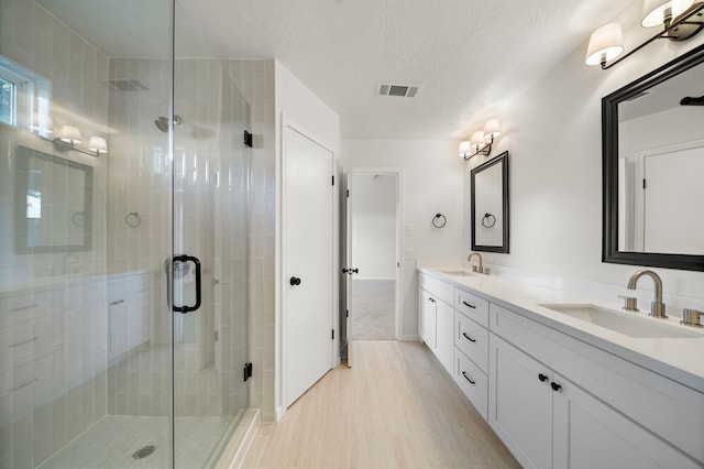 bathroom with vanity, an enclosed shower, a textured ceiling, and hardwood / wood-style flooring