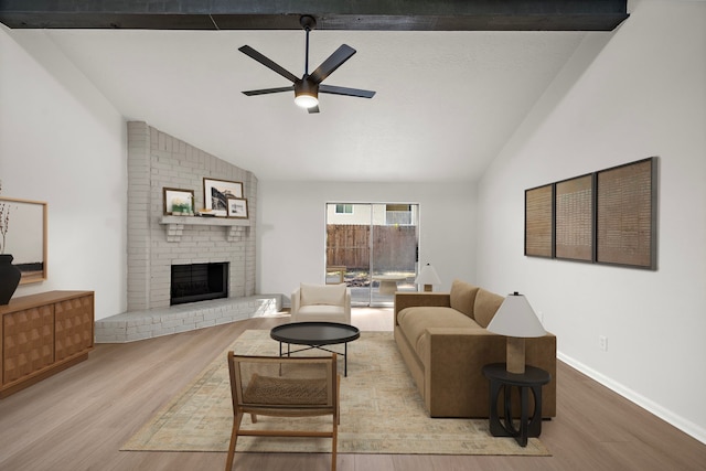 living room with vaulted ceiling with beams, a brick fireplace, ceiling fan, and light wood-type flooring