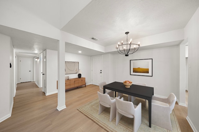 dining space featuring light hardwood / wood-style flooring, a textured ceiling, and an inviting chandelier