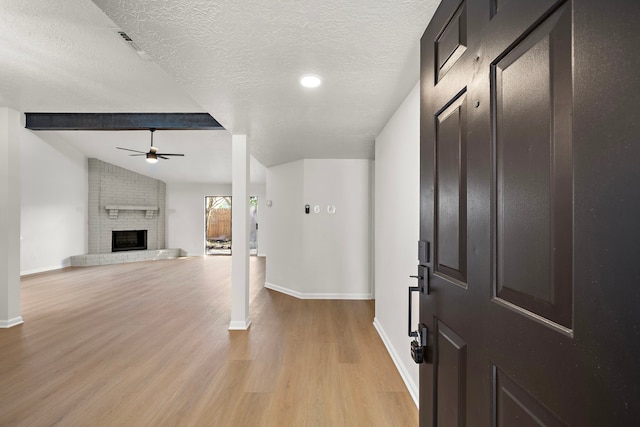 foyer featuring a textured ceiling, ceiling fan, a fireplace, vaulted ceiling with beams, and light hardwood / wood-style floors