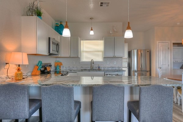 kitchen with a kitchen bar, appliances with stainless steel finishes, sink, decorative light fixtures, and light hardwood / wood-style floors