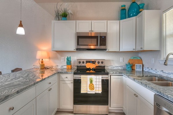 kitchen featuring appliances with stainless steel finishes, light stone counters, white cabinetry, and sink