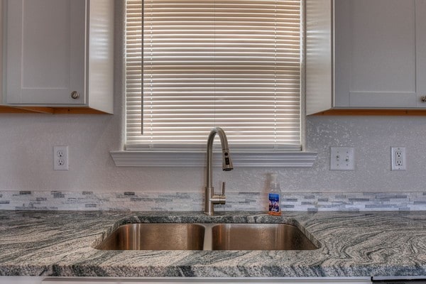 kitchen with white cabinets, tasteful backsplash, stone counters, and sink