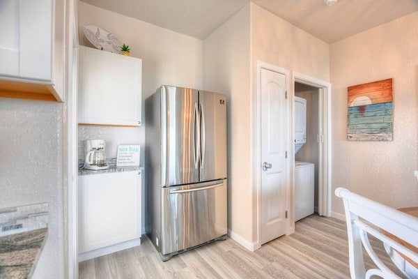 kitchen with white cabinetry, stainless steel fridge, stacked washer and dryer, and light hardwood / wood-style floors