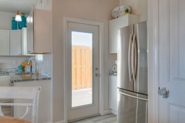 kitchen featuring stainless steel fridge, light stone countertops, light wood-type flooring, decorative light fixtures, and white cabinetry