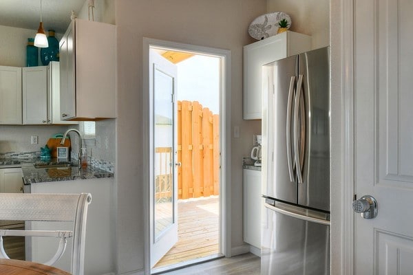 kitchen with decorative light fixtures, stainless steel fridge, dark stone countertops, and white cabinetry