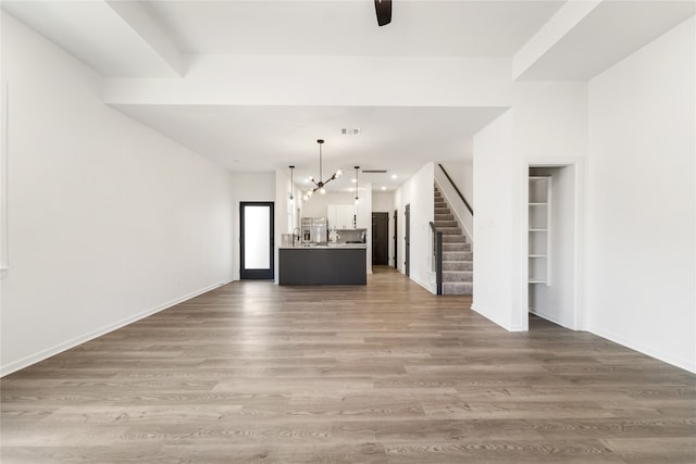 unfurnished living room featuring ceiling fan with notable chandelier and dark wood-type flooring