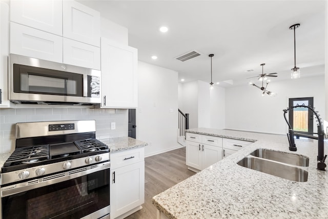 kitchen with stainless steel appliances, sink, light hardwood / wood-style flooring, white cabinets, and hanging light fixtures