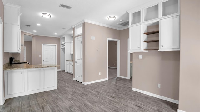 kitchen featuring white cabinets, crown molding, light stone counters, and hardwood / wood-style floors