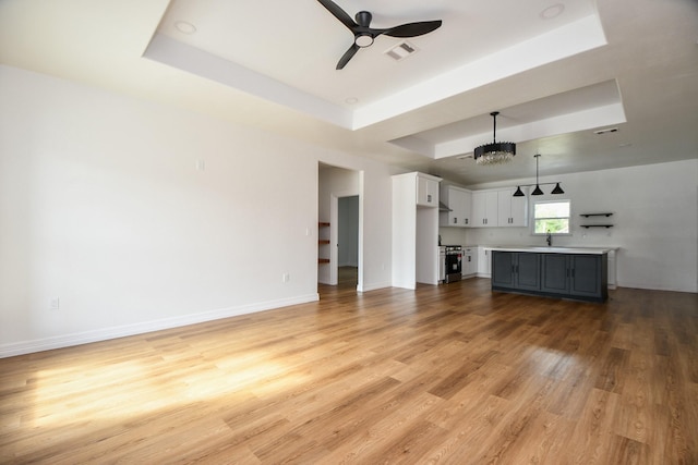 unfurnished living room with ceiling fan with notable chandelier, light hardwood / wood-style floors, a raised ceiling, and sink