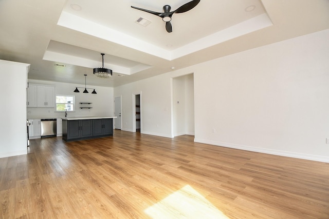 unfurnished living room with ceiling fan with notable chandelier, light hardwood / wood-style flooring, a raised ceiling, and sink