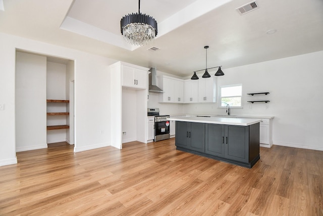 kitchen with decorative light fixtures, light hardwood / wood-style flooring, white cabinets, stainless steel stove, and a kitchen island