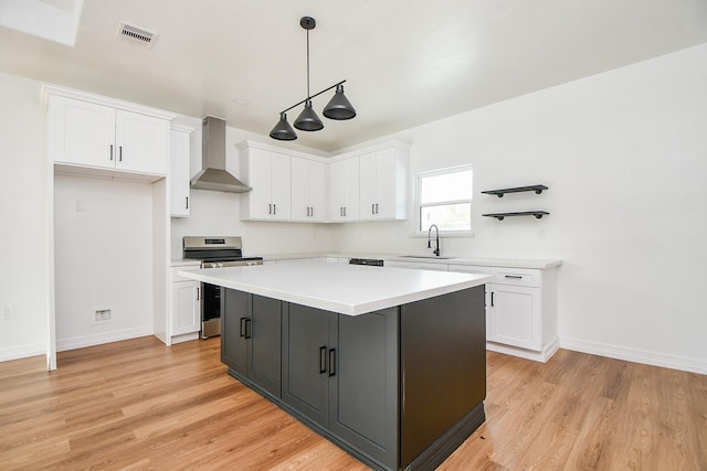 kitchen featuring stainless steel range oven, white cabinets, and wall chimney range hood