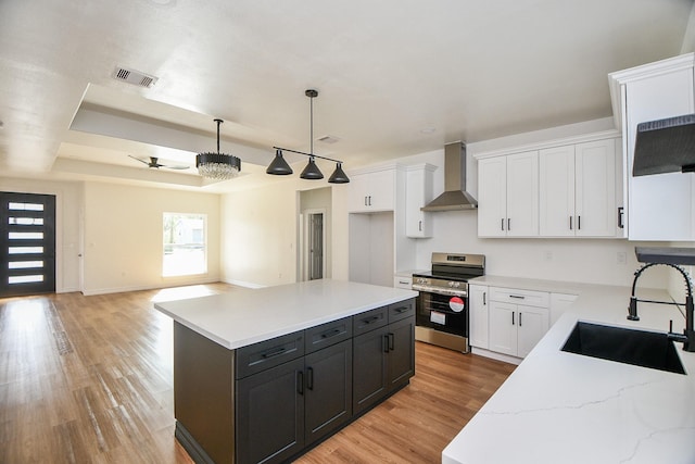 kitchen with white cabinetry, stainless steel range, a center island, sink, and wall chimney range hood