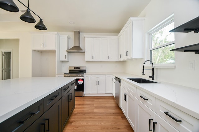 kitchen with white cabinets, wall chimney range hood, sink, hanging light fixtures, and appliances with stainless steel finishes