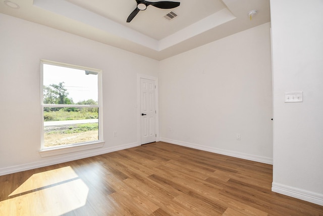 empty room with a tray ceiling, ceiling fan, and light hardwood / wood-style flooring