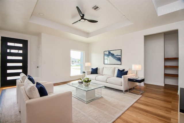 living room featuring ceiling fan, wood-type flooring, and a tray ceiling