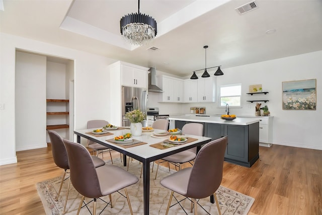 dining space with light wood-type flooring, sink, a tray ceiling, and an inviting chandelier