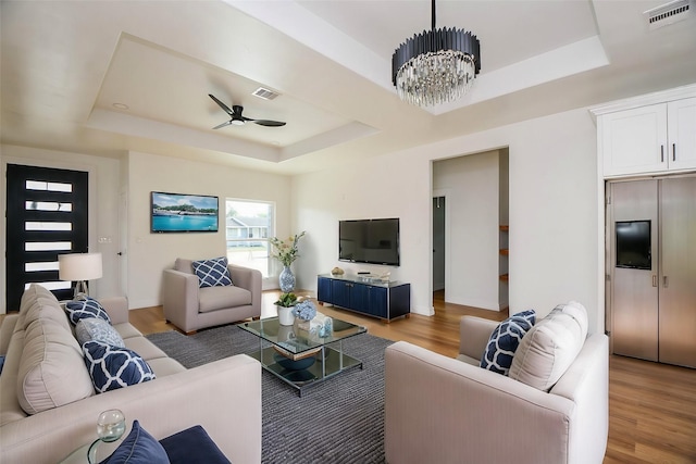 living room featuring ceiling fan with notable chandelier, light hardwood / wood-style flooring, and a tray ceiling