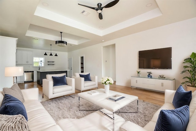 living room featuring light hardwood / wood-style flooring, ceiling fan, and a tray ceiling