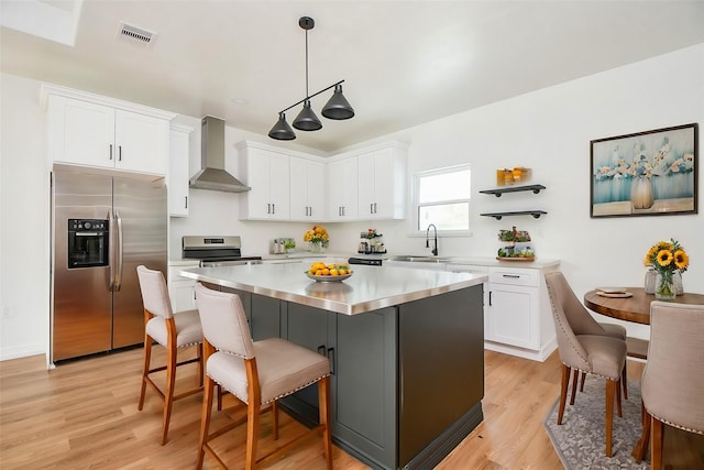 kitchen with appliances with stainless steel finishes, pendant lighting, white cabinetry, a center island, and wall chimney range hood