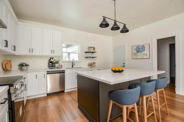 kitchen featuring sink, white cabinetry, a center island, hanging light fixtures, and appliances with stainless steel finishes