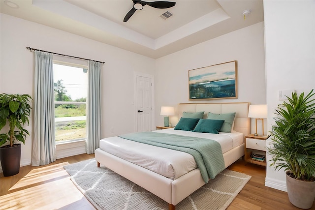 bedroom with a raised ceiling, ceiling fan, and light hardwood / wood-style floors