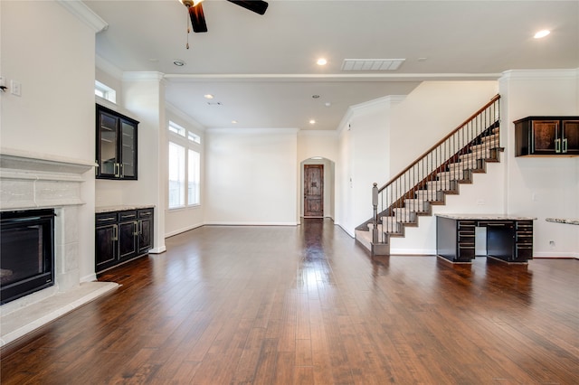 unfurnished living room with ornamental molding, ceiling fan, dark wood-type flooring, and a tiled fireplace