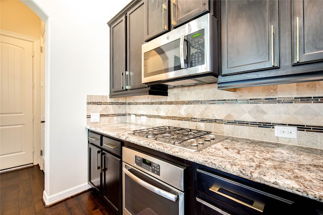 kitchen featuring light stone countertops, appliances with stainless steel finishes, dark hardwood / wood-style flooring, tasteful backsplash, and dark brown cabinets