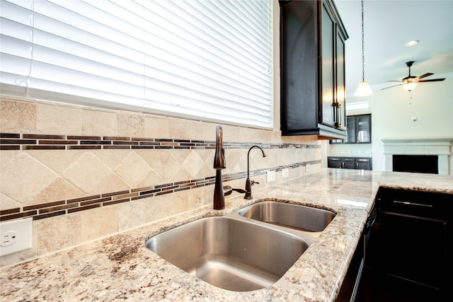 kitchen with ceiling fan, sink, light stone counters, decorative light fixtures, and decorative backsplash