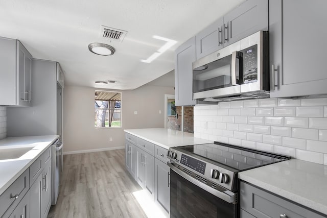 kitchen with tasteful backsplash, gray cabinets, light hardwood / wood-style floors, and appliances with stainless steel finishes