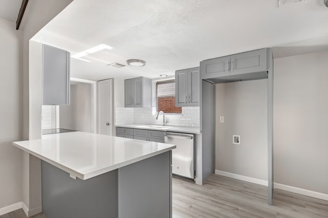 kitchen featuring light wood-type flooring, tasteful backsplash, stainless steel dishwasher, gray cabinetry, and a textured ceiling