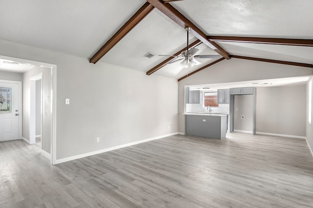 unfurnished living room featuring a textured ceiling, ceiling fan, sink, lofted ceiling with beams, and hardwood / wood-style flooring