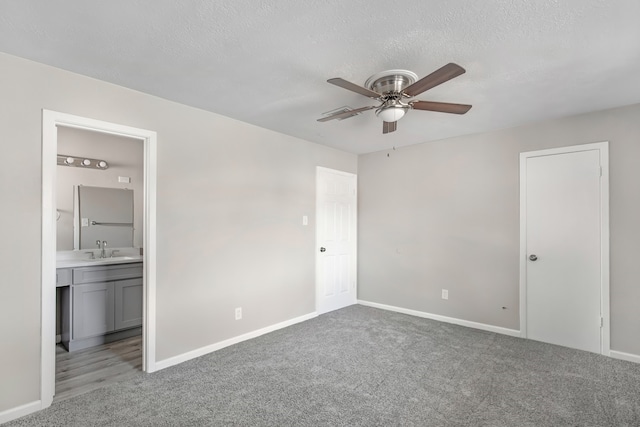 unfurnished bedroom featuring ensuite bathroom, sink, ceiling fan, a textured ceiling, and light colored carpet