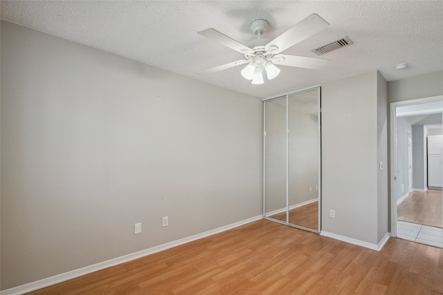 unfurnished bedroom featuring ceiling fan, a closet, light hardwood / wood-style floors, and a textured ceiling