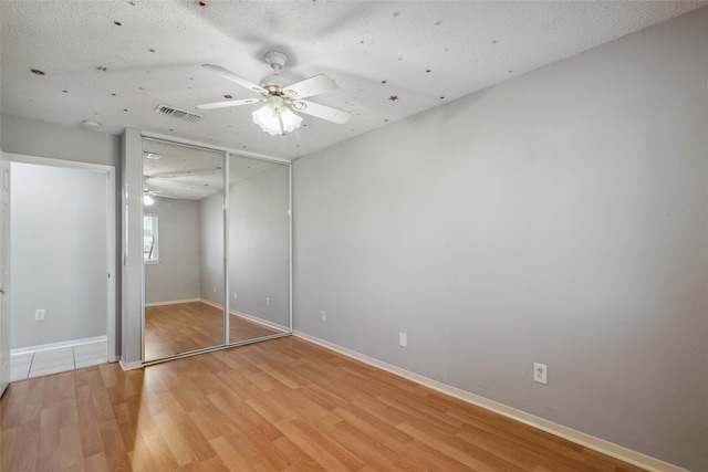 unfurnished bedroom featuring a textured ceiling, light hardwood / wood-style floors, a closet, and ceiling fan