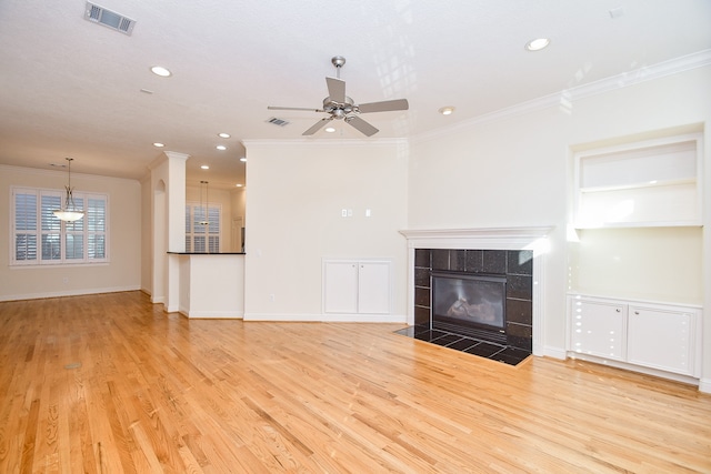 unfurnished living room with light hardwood / wood-style floors, crown molding, and a tiled fireplace